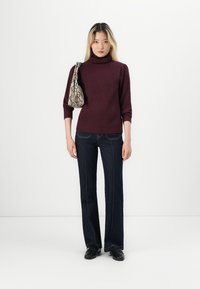 Burgundyröd ribbad polotröja kombinerad med mörkblå jeans med utsvängda ben. Mönstrad handväska i svart och vitt med textur. Svarta skor.