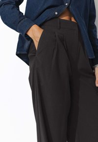 Pantalons noirs à rayures avec plis, dotés d'une taille haute, de poches latérales et d'une texture douce, associés à une chemise en denim.