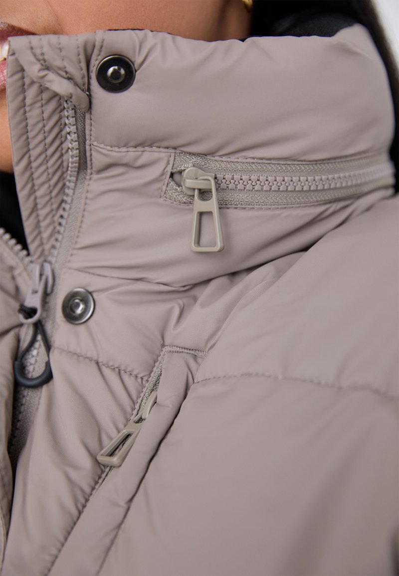 Light gray puffy jacket collar featuring a zipper and snap fasteners, with textured fabric and stitching details.