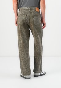 Lightly washed, olive green denim jeans with a relaxed fit, featuring a leather patch on the waistband and two back pockets.