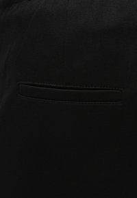 Czarne spodnie o gładkiej fakturze, z płaską tylną kieszenią o prostokątnym otworze i przeszyciami wzdłuż krawędzi.