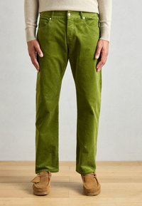Grønne kordfløjspants med lige snit, featuring fem lommer, metalnitter og en struktureret overflade, parret med brune mokkasiner.