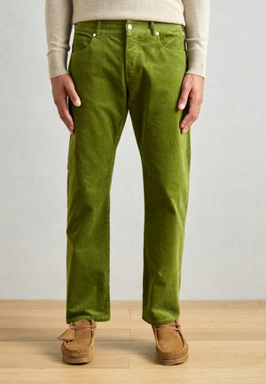 Grüne Cordhosen mit geradem Schnitt, ausgestattet mit fünf Taschen, Metallnieten und einer strukturierten Oberfläche, kombiniert mit braunen Mokassins.
