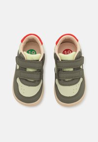 Green and beige toddler sneakers with red accents, featuring two Velcro straps, rounded toe, and a cushioned insole. Size markers visible inside.