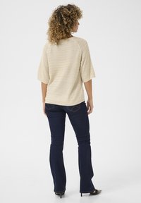 T-shirt en maille beige avec un motif texturé et rayé, à manches trois-quarts. Assorti avec un jean évasé bleu foncé et des chaussures à talons noires.