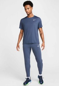 Navy athletic t-shirt with a crew neck and white logo; paired with matching tapered pants. Textured material and blue sneakers with green accents.
