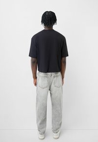 Svart kortärmad t-shirt i kombination med ljusgrå, löst sittande jeans. Jeansen har bakfickor och en urtvättad textur, kompletterat med vita sneakers.