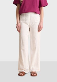 White, wide-leg pants with textured square patterns, paired with a loose, purple top. Brown sandals adorn the feet.