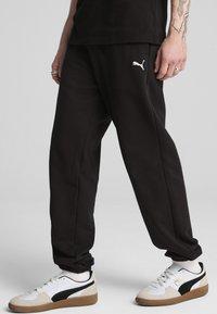 Zwarte sweatpants van katoen, met een elastische tailleband en een wit Puma-logo. Gepaard met witte en zwarte Puma sneakers.