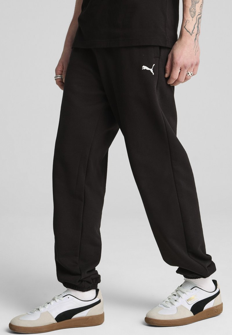 Zwarte sweatpants van katoen, met een elastische tailleband en een wit Puma-logo. Gepaard met witte en zwarte Puma sneakers.