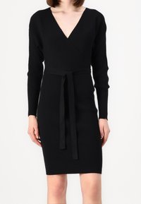Abito nero lavorato a maglia con scollatura a V profonda, maniche lunghe e una cintura annodata in vita, con una texture a coste e una forma aderente.