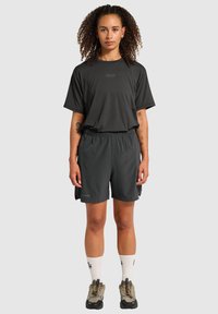 Czarny górny element sportowy oraz spodenki wykonane z lekkiego materiału, charakteryzujące się luźnym krojem, z białymi skarpetkami i szarymi sneakersami.