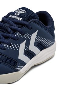 Marineblauer Sportschuh mit Mesh-Obermaterial, weißem Logo und Chevron-Design, gepolstertem Kragen und weißer Sohle, mit gepunkteten Akzenten nahe der Basis.