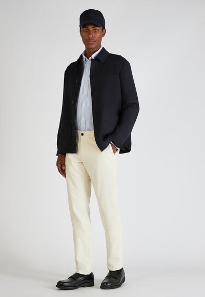 Giacca blu marina con bottoni, camicia a righe blu chiaro, pantaloni in corduroy color crema e scarpe in pelle nere. Design minimalista, vestibilità su misura.