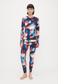 Večbarvna aktivna obleka, ki vključuje dolg rokav in legice. Tkanina ima gladko, raztegljivo teksturo z oblaki v modri, oranžni in roza barvi.