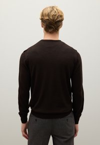 Maglione a maglia marrone con maniche lunghe e scollatura a girocollo, caratterizzato da una texture liscia e polsini a coste. Indossato con pantaloni grigio scuro.