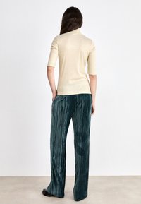 T-shirt beige à col roulé et à manches courtes avec un design ajusté. Pantalons à larges rayures teal fabriqués dans un tissu texturé.