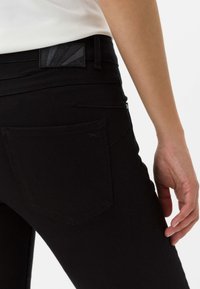 Zwarte denim jeans met een getailleerd ontwerp, voorzien van een achterzak en een getextureerde tailleband met een geometrisch patroon.