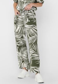 Groene wijde broek met een wit tropisch bladenpatroon en een strikband in de taille. Gecombineerd met een ontspannen top en witte sneakers.