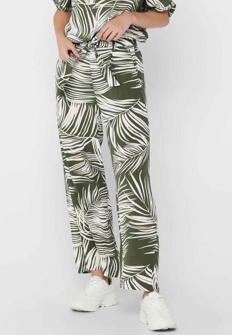 Groene wijde broek met een wit tropisch bladenpatroon en een strikband in de taille. Gecombineerd met een ontspannen top en witte sneakers.