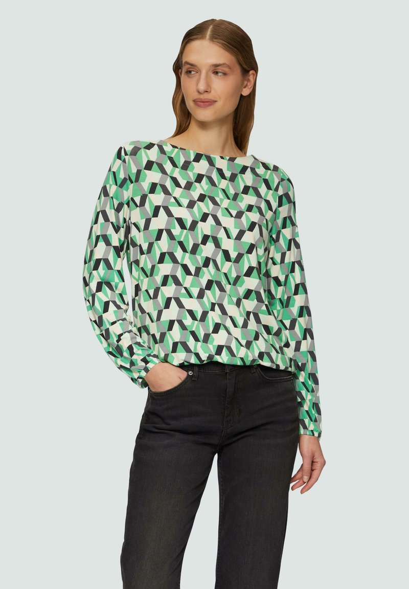 Langsleeve, geometrisch patroon blouse in groen, wit en zwart, gecombineerd met donkere jeans; heeft een ronde halslijn en een relaxte pasvorm.
