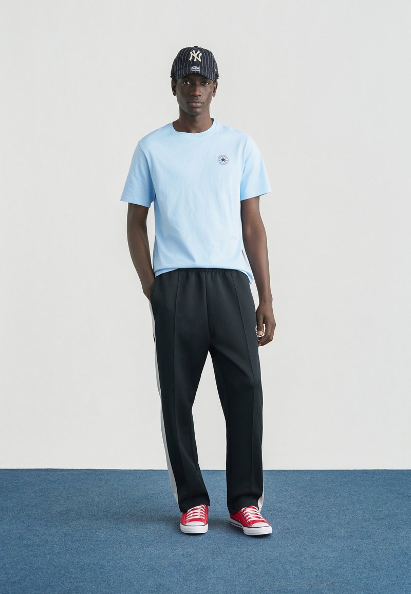 Lyseblå bomuld T-shirt med et lille logo, kombineret med sorte joggingbukser med hvide sidestriber og røde sneakers.