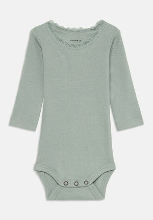 Body per bambini a maniche lunghe, di colore verde chiaro, in cotone a costine. Presenta un collo rifinito con pizzo e chiusure a pressione sul fondo. Materiale morbido.