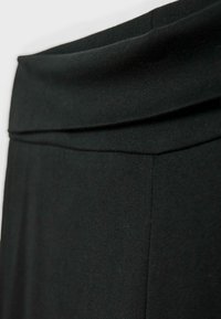 Crna, rastezljiva tkanina s preklopnim pojasom. Glatka tekstura koja ističe čistu siluetu i minimalne detalje šivanja.