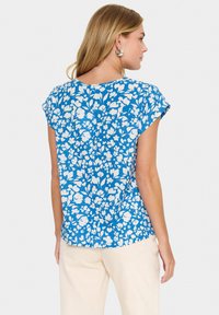 Blusa a maniche corte di un blu brillante con motivo floreale bianco, con scollo rotondo e vestibilità rilassata. Materiale in cotone morbido.