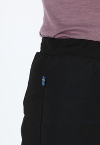 Black track pants feature a seamless design and an elastic waistband, with a small blue and yellow Swedish flag accent on the side.