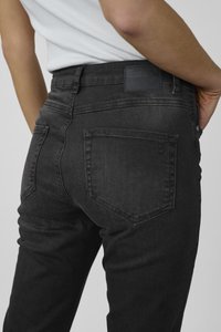 Black denim jeans with a slim fit, featuring a back pocket design and a textured waistband label. Stitched accents enhance structure.