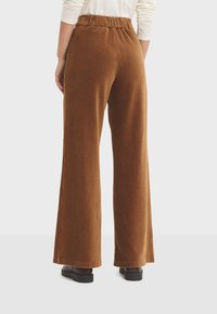 Brown corduroy wide-leg pants with a ribbed texture, featuring an elastic waistband and a relaxed fit. No pockets visible in the image.