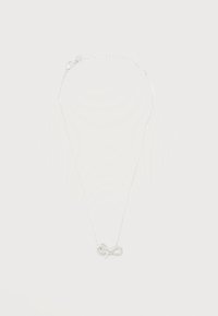 Λεπτή ασημένια αλυσίδα με ένα μικρό, λαμπερό μενταγιόν σε σχήμα φιόγκου στο κέντρο σε απλό λευκό φόντο.