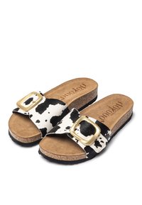 Zwart-wit koeienprint slide sandalen met grote gouden gesp, kurken voetbed en gestructureerde tan binnenzool. Zwart rubberen buitenzool voor grip.