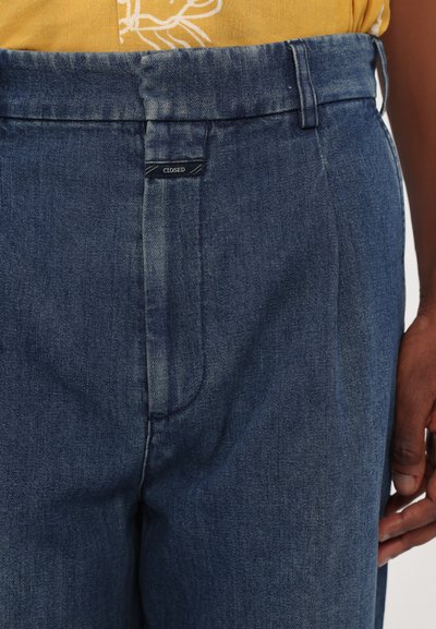 Mørkeblå denimbukser med høy midje, med glidelås, beltehemper og en liten logo-tag på frontlinningen.