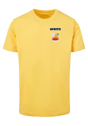 Geltona medvilnės marškinėliai su mėlynu "SPRITZ" tekstu ir gėrimo su apelsino riekelė grafika kairėje krūtinės pusėje.