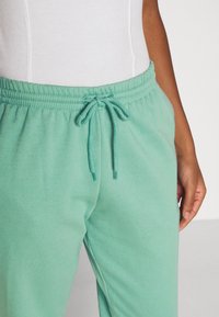 Lichtgroene joggingsbroek gemaakt van zachte stof, met een elastische tailleband met trekkoord en zijzakken. Soepele, relaxte pasvorm.