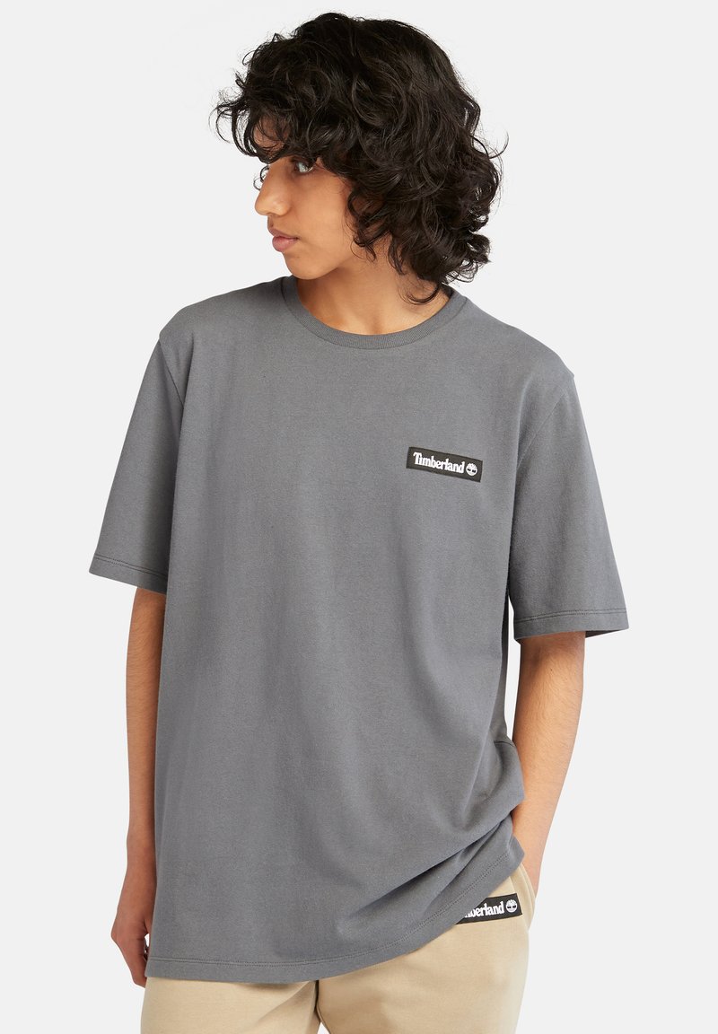 T-shirt in cotone grigio con collo rotondo e maniche corte, caratterizzata da un piccolo logo patch nero di Timberland sul petto e sull'orlo laterale.