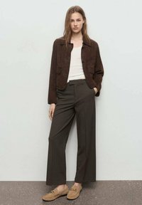 Giacca corta in suede marrone, canotta bianca, pantaloni larghi marrone scuro e mocassini beige. Texture lisce con minimal hardware.