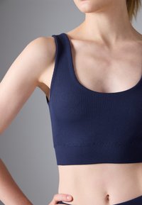 Sutien sportiv din material în dungi de culoare bleumarin, cu bretele late. Textură fină, design ajustat și decolteu rotund, având o bandă sub bust fără cusături.