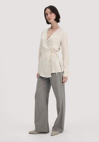 Blusa avvolgente crema con maniche lunghe e dettaglio con fiocco, abbinata a pantaloni grigi a gamba larga e ballerine beige a punta. Texture semplici e lisce.