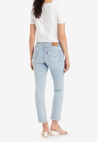 Jeans de pierna recta azul claro con una textura deslavada, dos bolsillos en la parte posterior y un parche de cuero en la cinturilla. Combinados con una blusa blanca de manga corta.