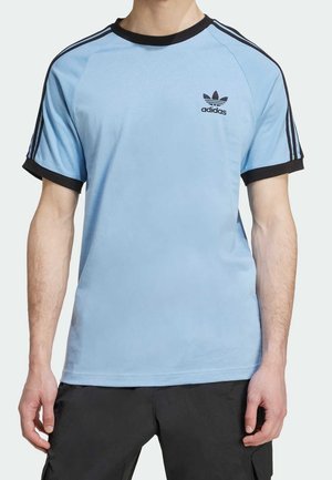 T-shirt en coton bleu clair avec accents noirs, doté d'un col rond côtelé, de manches raglan courtes, et d'un petit logo Adidas noir sur la poitrine.