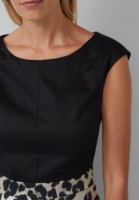 Haut sans manches noir avec un décolleté large et des détails de couture, associé à une jupe à motifs présentant un fond clair et des taches de léopard foncées.
