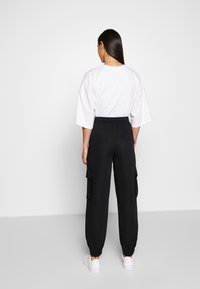 Vit oversized t-shirt i kombination med svarta cargobyxor med sidofickor och elastiska mudd. Modellen bär vita skor.