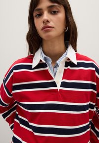 Rood en wit gestreepte polo met een witte kraag en een blauw-wit gestreepte binnenkraag, gemaakt van zacht katoen.