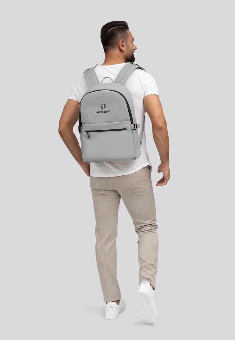 Zaino grigio con una superficie liscia, tasca anteriore con zip, spallacci imbottiti e il logo del marchio ben in evidenza.