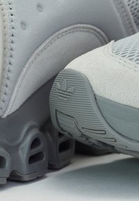 Chaussures de sport grises avec un dessus en maille, des accents en daim et une semelle en caoutchouc texturé. Comprend un logo à l'arrière et des trous de ventilation.