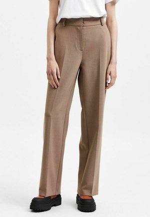 Braune maßgeschneiderte Hosen mit hoher Taille, geraden Beinen und subtilen vertikalen Nähten. Kombiniert mit schwarzen Plateau-Schuhen.