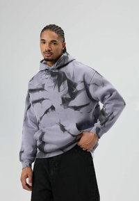 Lichtpaarse hoodie met een zwart tie-dye patroon, gemaakt van zacht materiaal met een voorzak en een capuchon met trekkoord.
